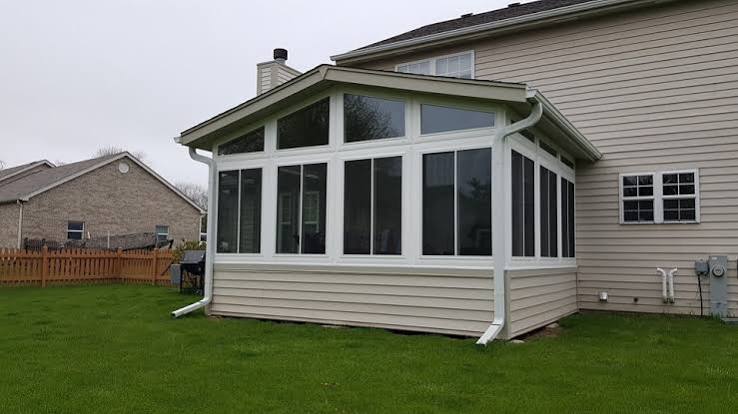Four-season sunroom addition with white trim and large glass windows attached to a home
